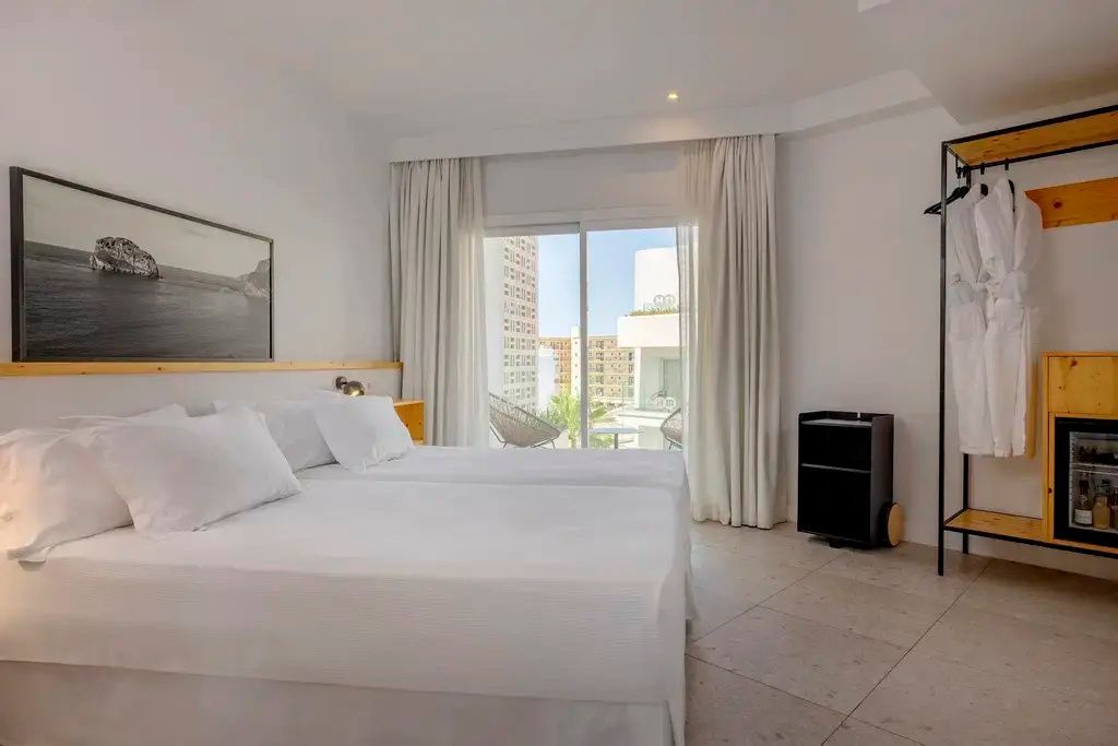 Helles Schlafzimmer im Hotel mit Doppelbett und Zugang zum Balkon durch eine Glastür.