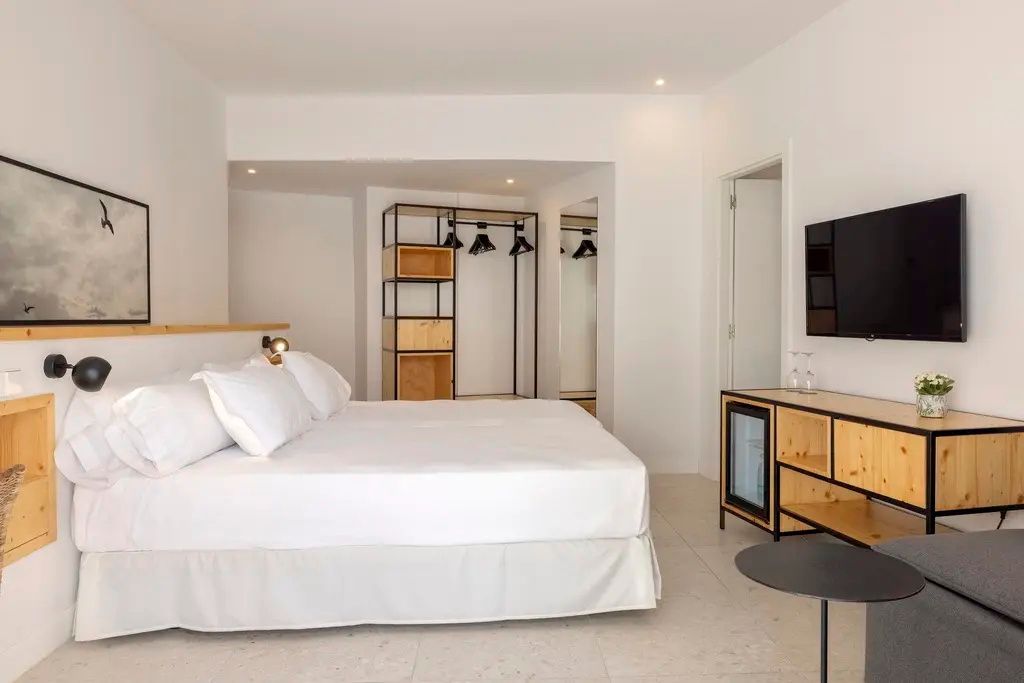 Modern eingerichtetes Hotelzimmer mit Doppelbett, Fernseher und offenem Kleiderschrank.