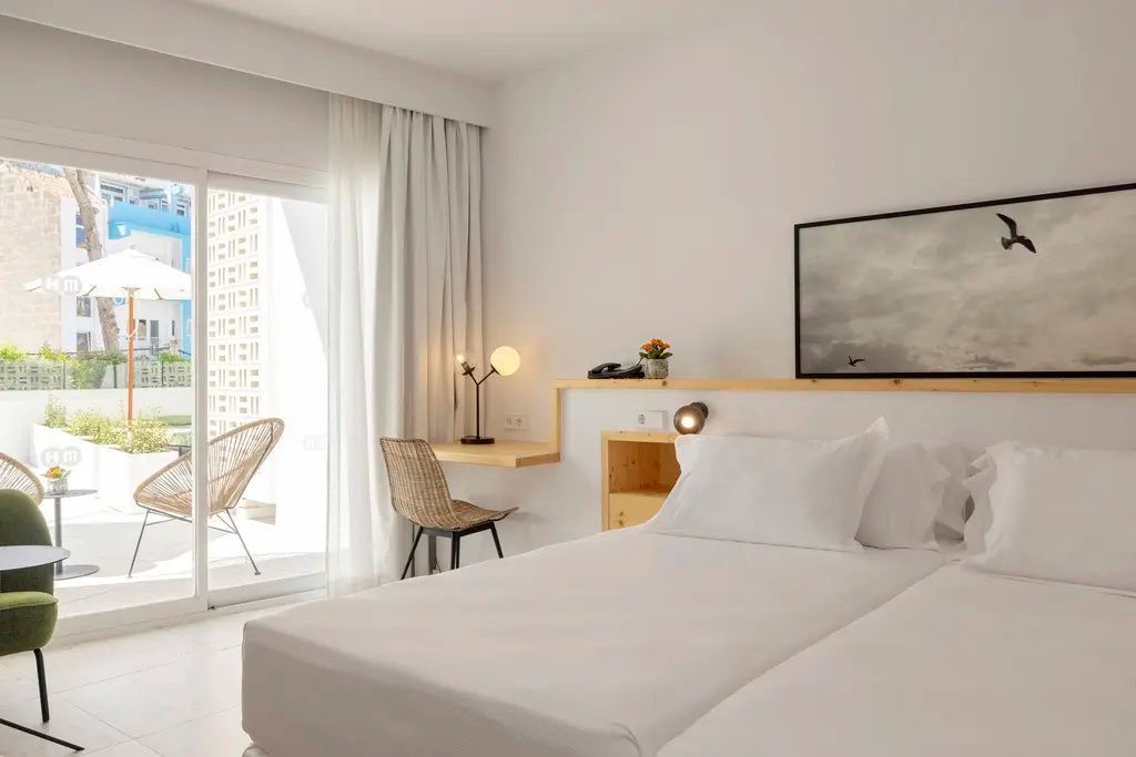 Helles Hotelzimmer mit Doppelbett, kleinem Schreibtisch und Balkonzugang.