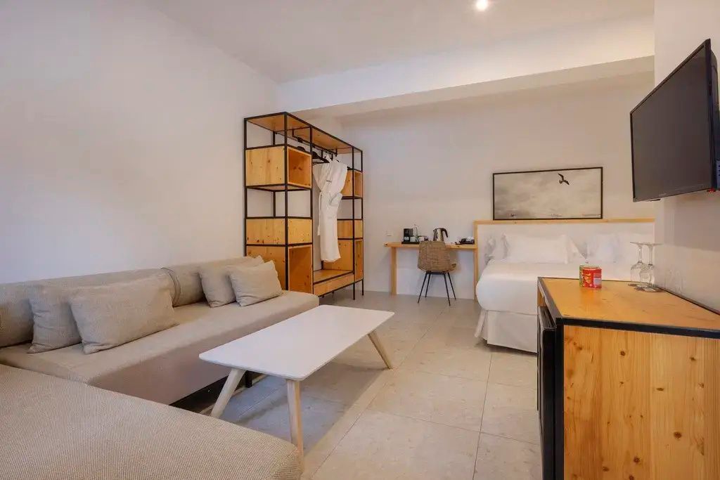Sitzbereich mit grauem Sofa und weissem Tisch sowie Doppelbett im Hotelzimmer.