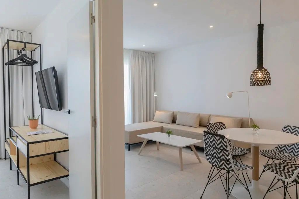 Heller Wohnbereich einer Suite mit beigem Ecksofa, Couchtisch und Sitzgruppe.