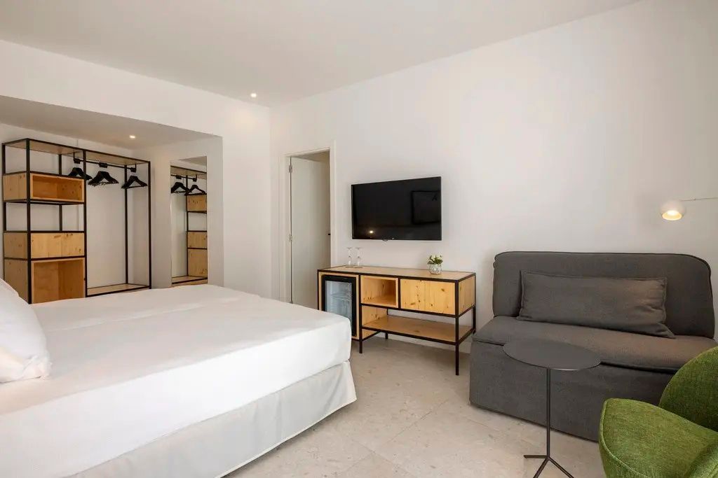 Hotelzimmer mit einem Doppelbett, einem grauen Sesselsitz und einer TV-Anrichte.