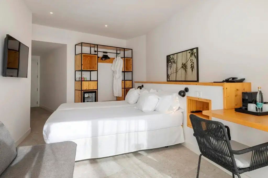 Hotelzimmer mit bezogenem Doppelbett, Schreibtisch und offenem Kleiderschrank aus Holz.