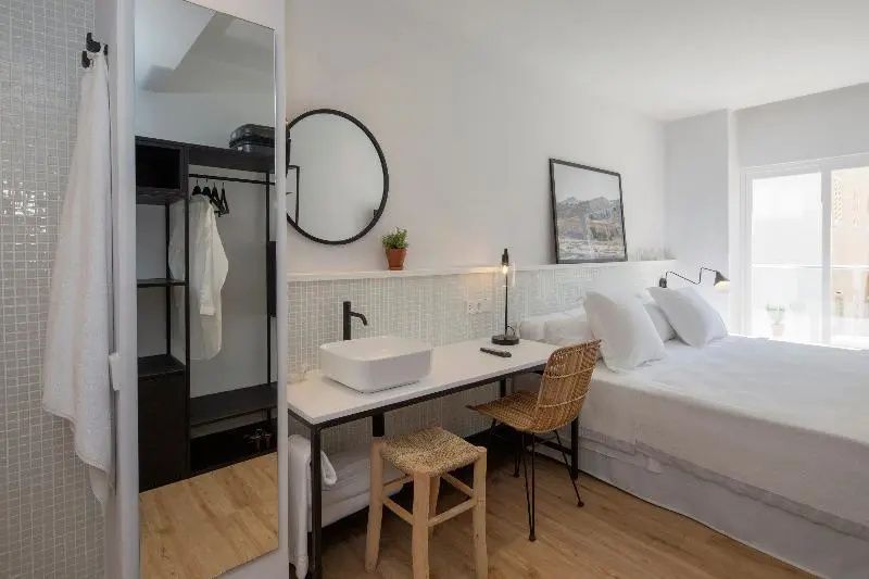 Helles Hotelzimmer mit weißem Doppelbett, Schreibtisch und integriertem Waschbecken.