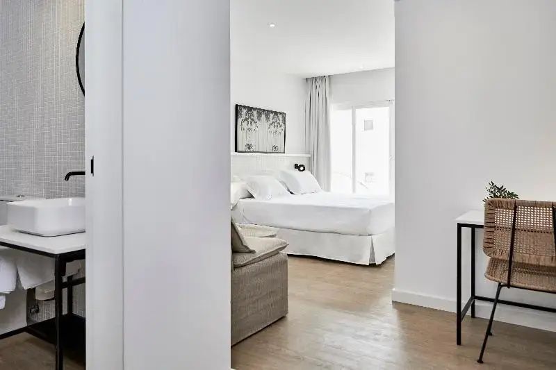 Blick in ein hell eingerichtetes Hotelzimmer mit weißem Doppelbett und großem Fenster.