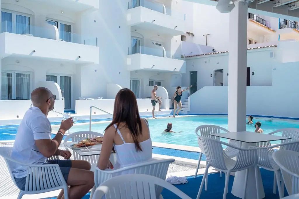 Außenpool im Innenhof eines weißen Gebäudes mit Sitzplätzen und Hotelgästen.