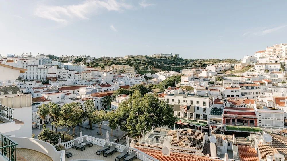 Blick von oben auf weiße Häuser, rote Dächer und grüne Hügel der Stadt Albufeira.