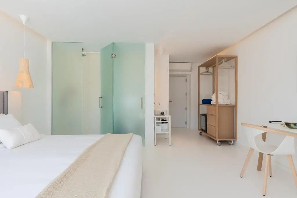 Weißes Zimmer mit einem offenen Kleiderschrank aus Holz und matten Glastüren zum Bad.