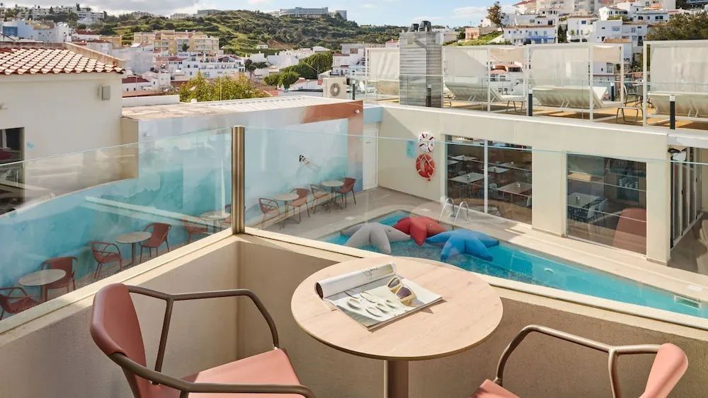 Blick vom Balkon mit Tisch auf einen Poolbereich mit Seestern-Schwimmkissen.