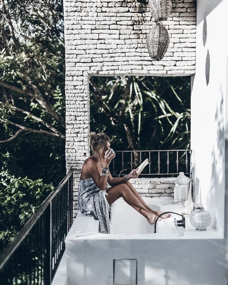 Frau sitzt auf dem Balkon einer mit hellen Backsteinen erbauten Terrasse und liest ein Buch.