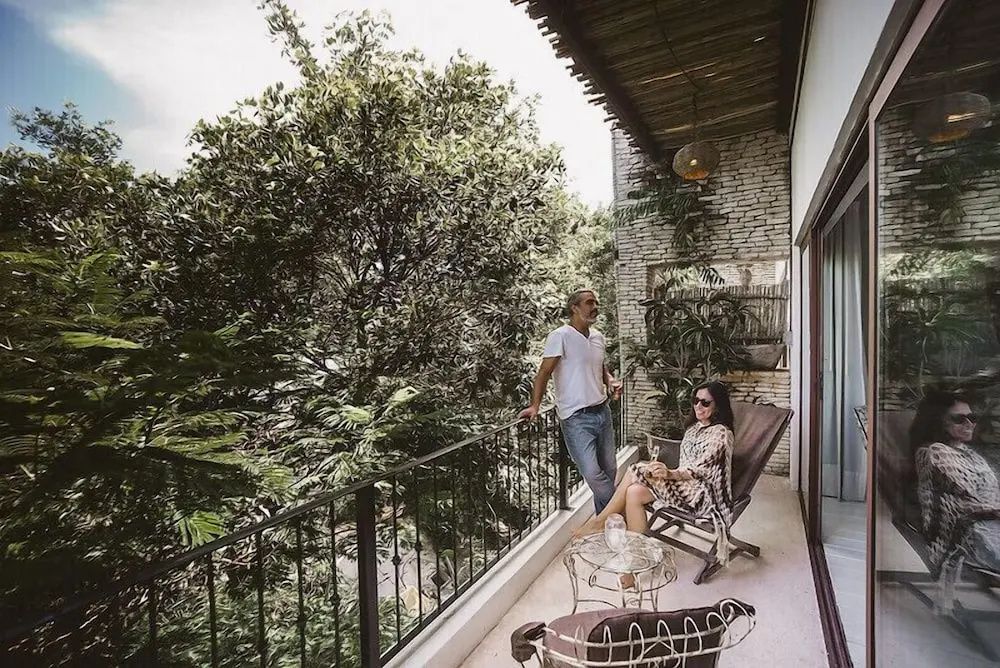 Paar entspannt auf einem überdachten Balkon mit Blick auf dichte grüne Bäume und Pflanzen.