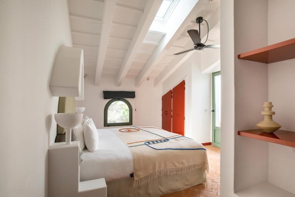 Hell gestaltetes Schlafzimmer mit Holzbalkendecke, Deckenventilator und Dachfenster.