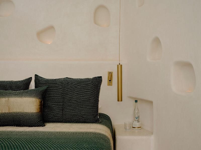 Bett mit grüner Tagesdecke neben einer hellen Wand mit beleuchteten Nischen