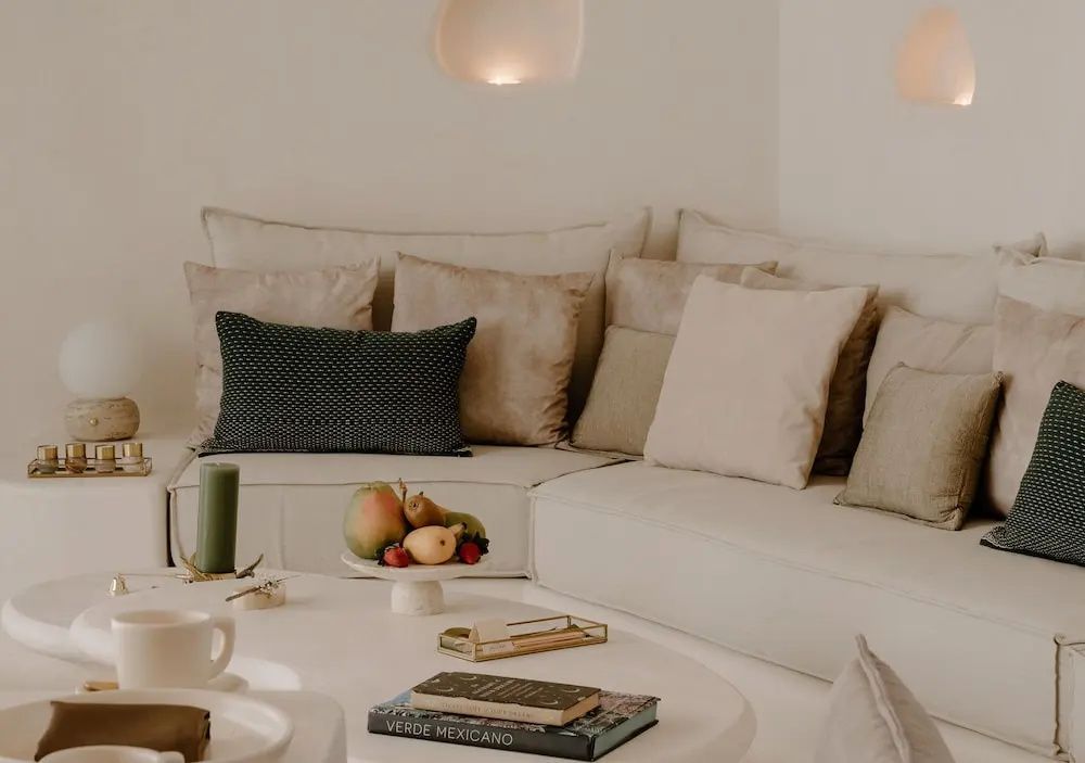 Helles Ecksofa mit zahlreichen Kissen und einem kleinen Couchtisch samt Obstschale.