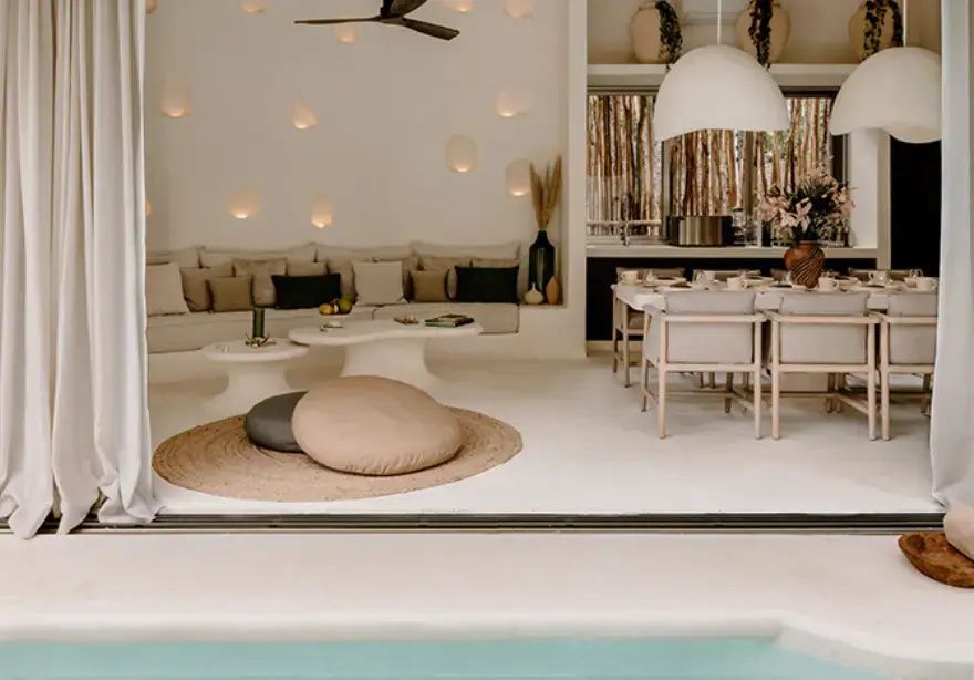 Helles Wohnzimmer mit beiger Couch, rundem Teppich und Ausblick auf das Poolbecken.
