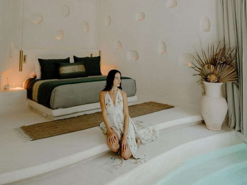Eine Frau sitzt am Rand eines kleinen Indoor-Pools im weiß gestalteten Schlafzimmer.
