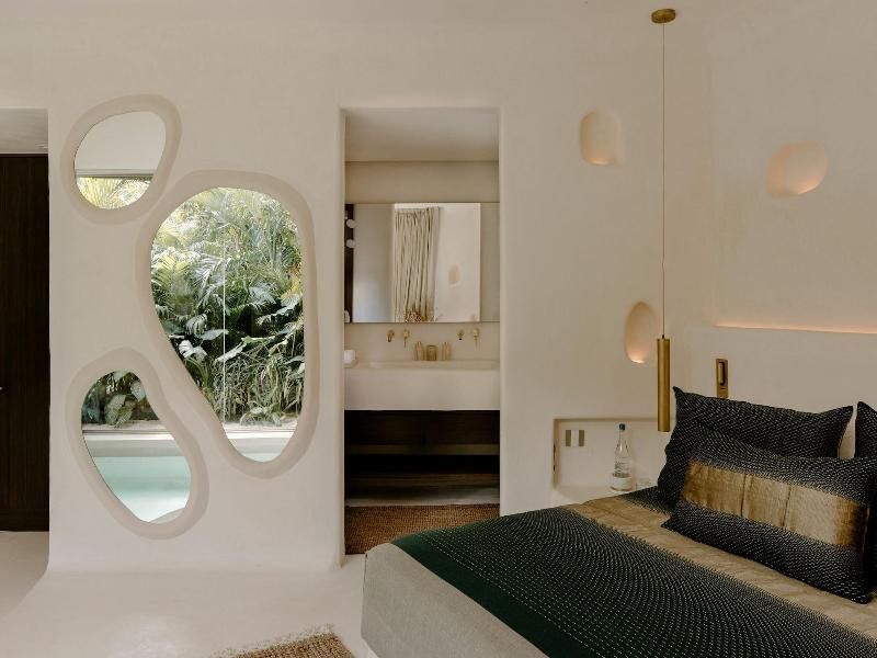 Schlafzimmer mit Blick durch organisch geformte Fenster auf den Außenbereich und ins Badezimmer.