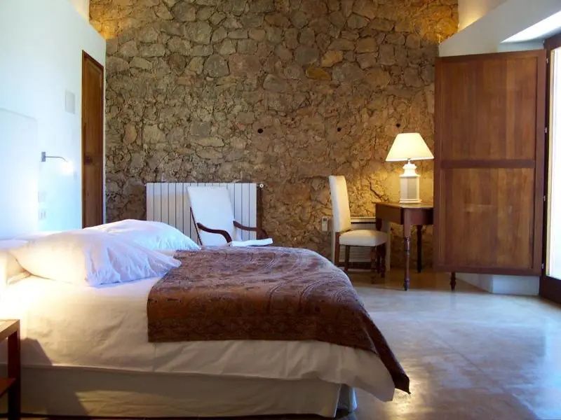 Rustikales Hotelzimmer mit Natursteinwand, Doppelbett und Schreibtisch.