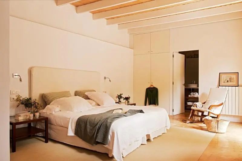Helles Schlafzimmer mit Holzbalkendecke, großem Doppelbett und Blick ins angrenzende Bad.