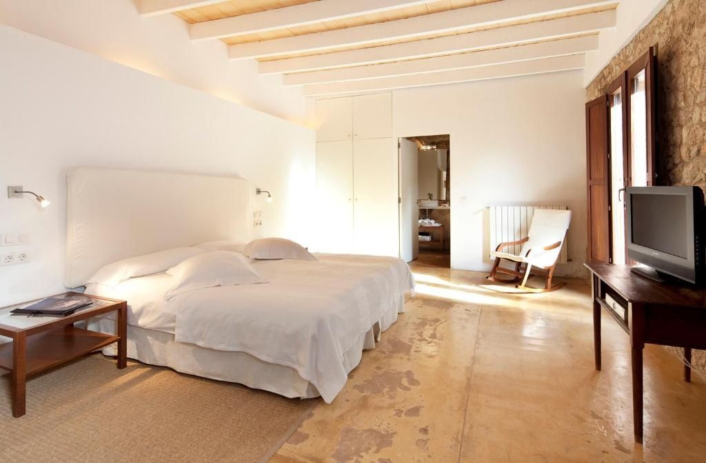 Sonnendurchflutetes Schlafzimmer mit Holzbalkendecke, Schaukelstuhl und hellem Doppelbett.