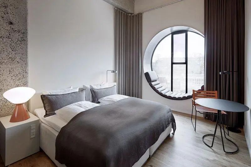 Hotelzimmer mit großem Doppelbett und einem markanten runden Fenster mit Sitznische.
