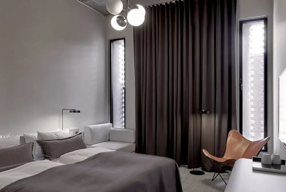 Hotelzimmer mit Doppelbett, dunklen Vorhängen und einem Sessel in der Ecke.