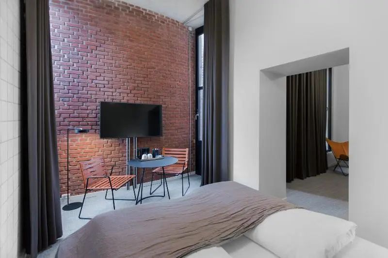 Hotelzimmer mit roter Backsteinwand, Fernseher und einer kleinen Sitzgruppe mit zwei Stühlen.