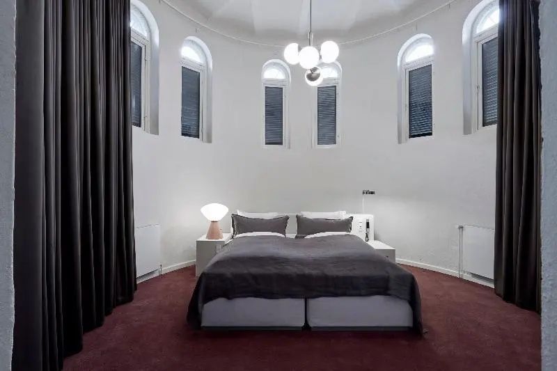 Rundes Schlafzimmer mit hohen Rundbogenfenstern, Doppelbett und dunklem Teppichboden.