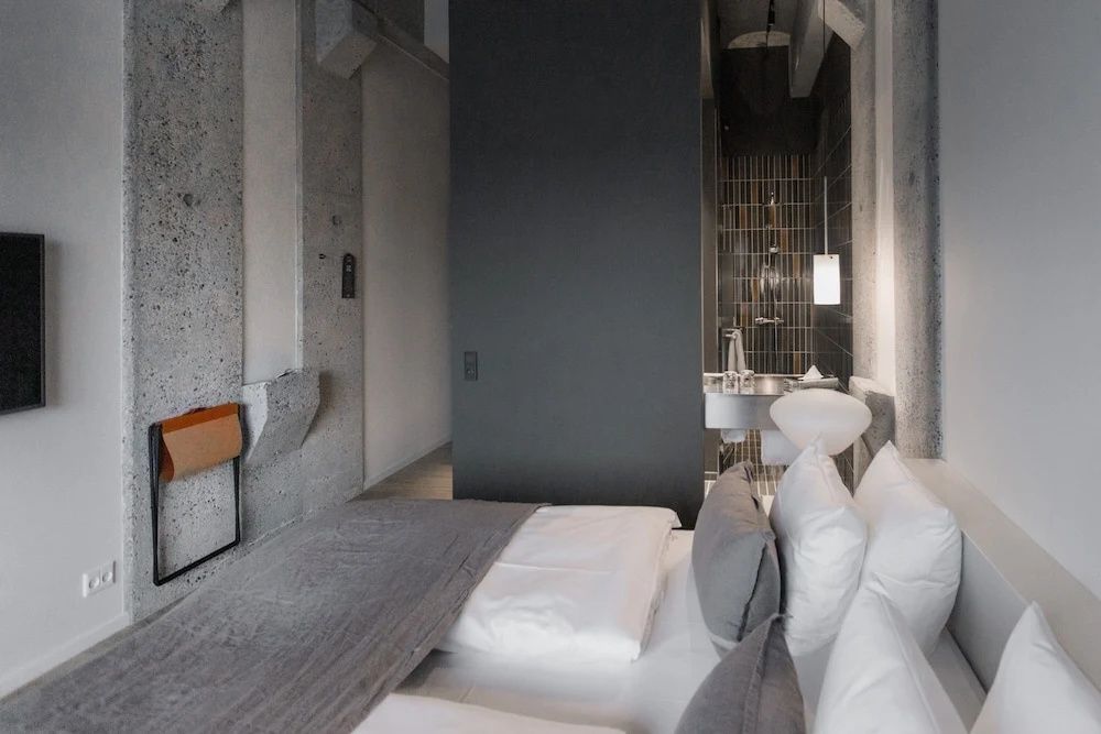Zimmer mit Blick vom Bett auf Sichtbetonwände und das angrenzende Badezimmer.