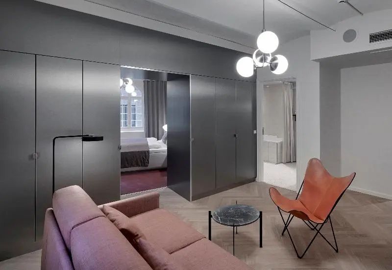 Sitzbereich einer Suite mit rosa Sofa, Lederstuhl und Blick in das angrenzende Schlafzimmer.