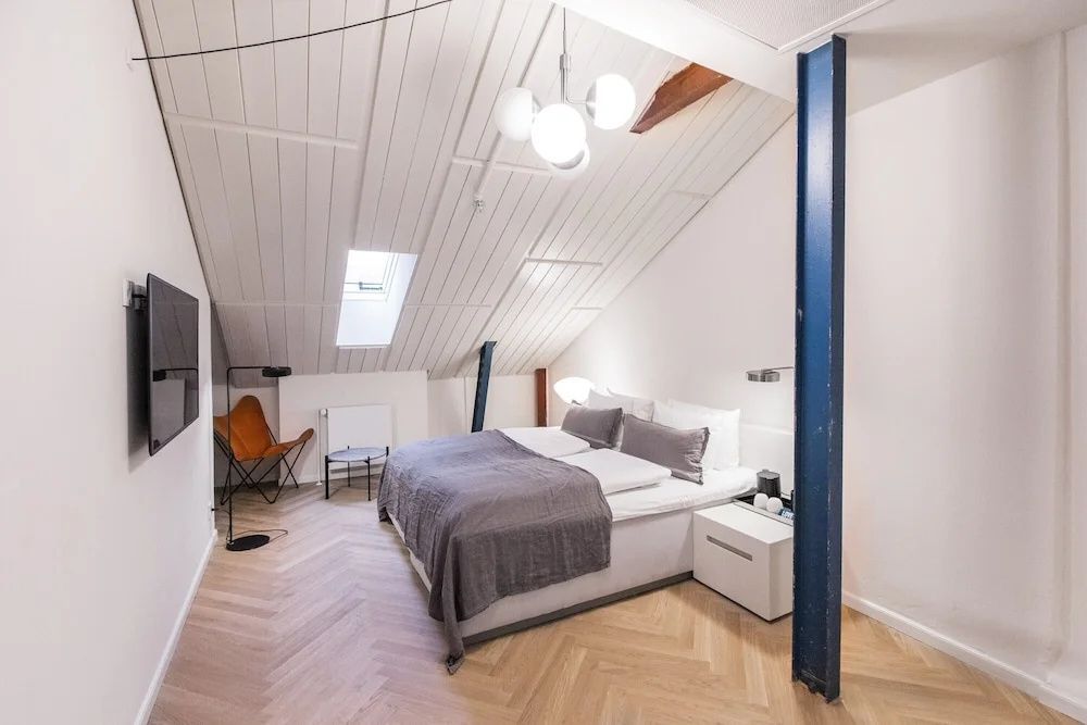 Doppelbett unter einer hellen Dachschräge mit Dachfenster und einem blauen Stahlträger