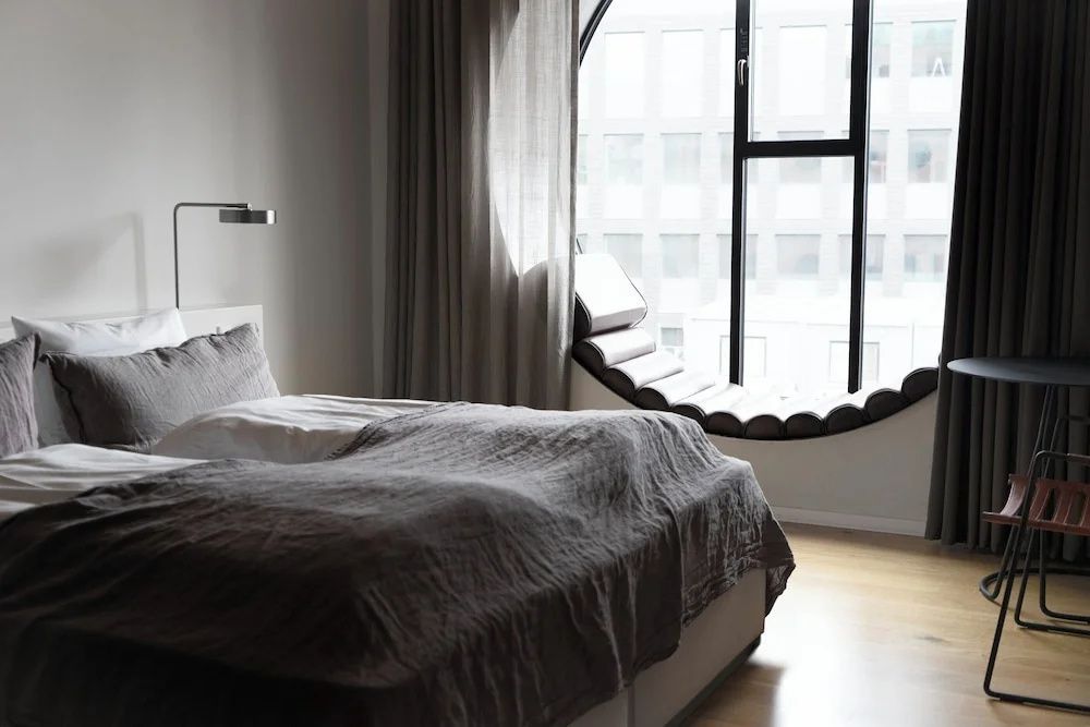 Hotelzimmer mit grauem Bett, rundem Fenster und einer integrierten Liegefläche im Rahmen.
