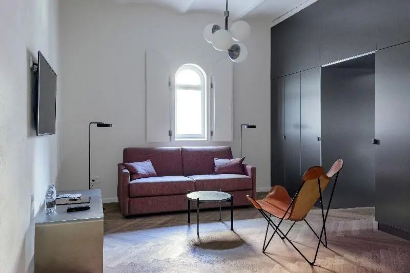 Sitzbereich im Zimmer mit rosa Sofa, Ledersessel und rundem Fenster mit Klappläden.