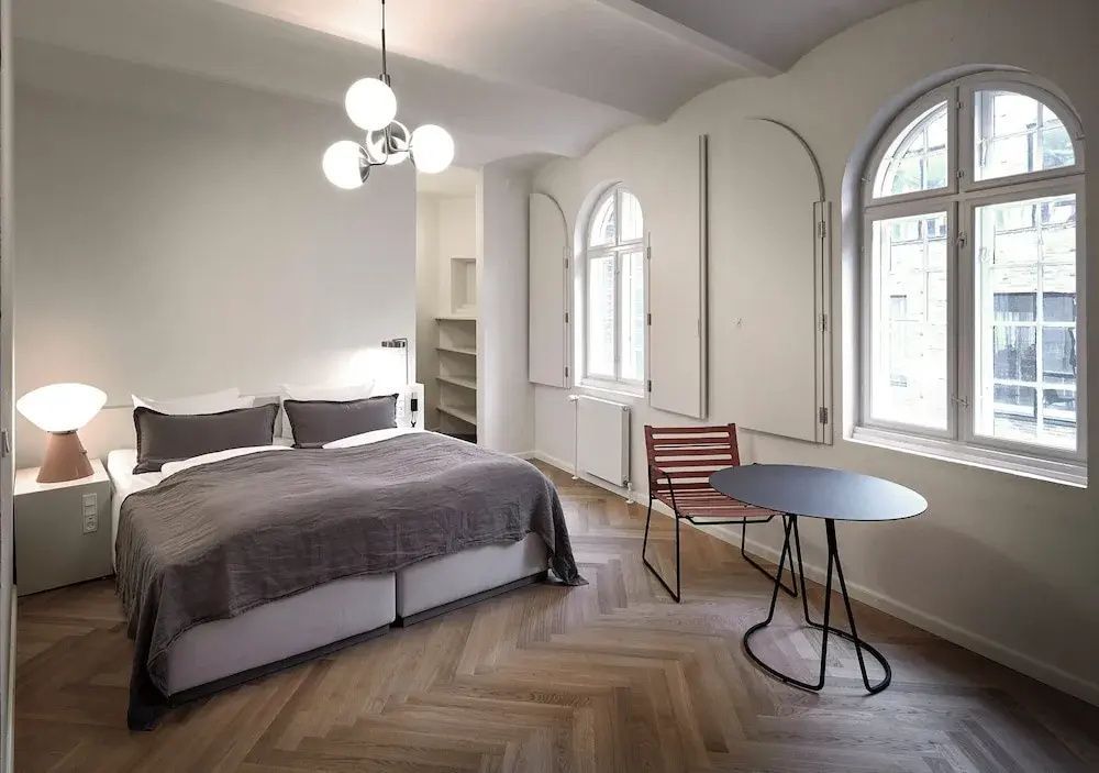 Modern eingerichtetes Hotelzimmer mit Doppelbett, Fischgrätparkett und Rundbogenfenstern.