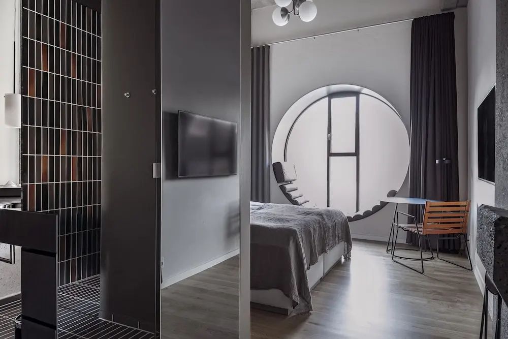 Blick in ein Hotelzimmer mit Fernseher an der Wand, Doppelbett und rundem Panoramafenster.