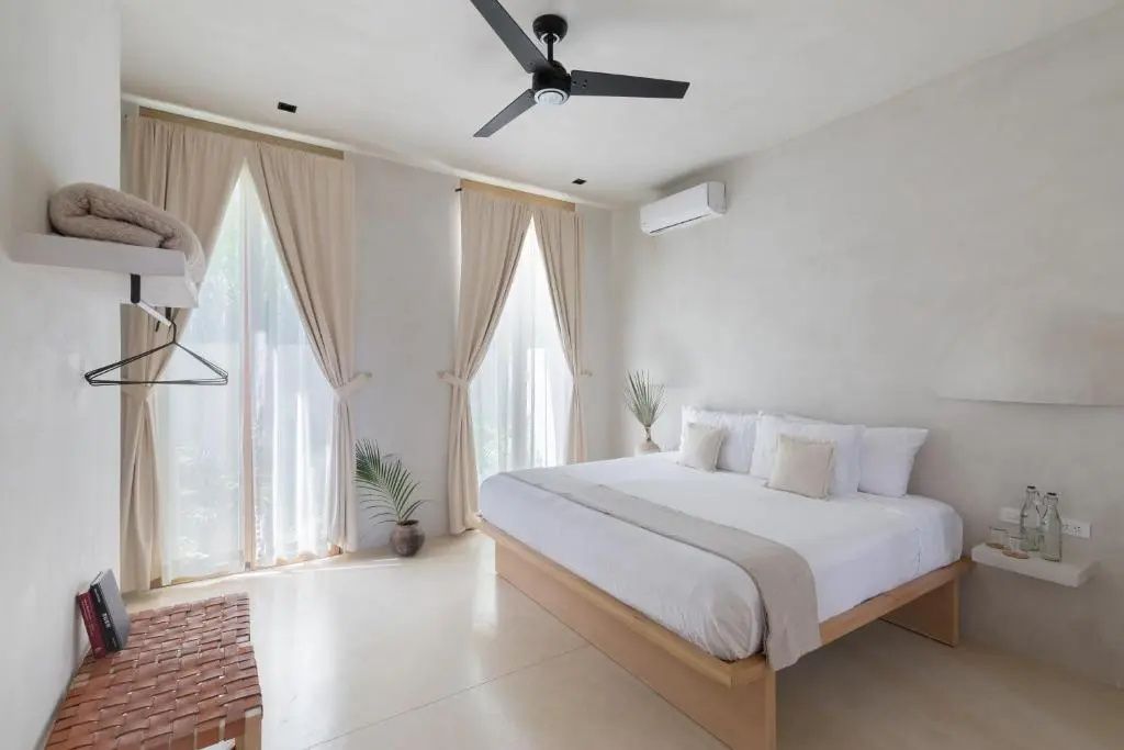 Helles Hotelzimmer mit Doppelbett aus Holz, Deckenventilator und Vorhängen.