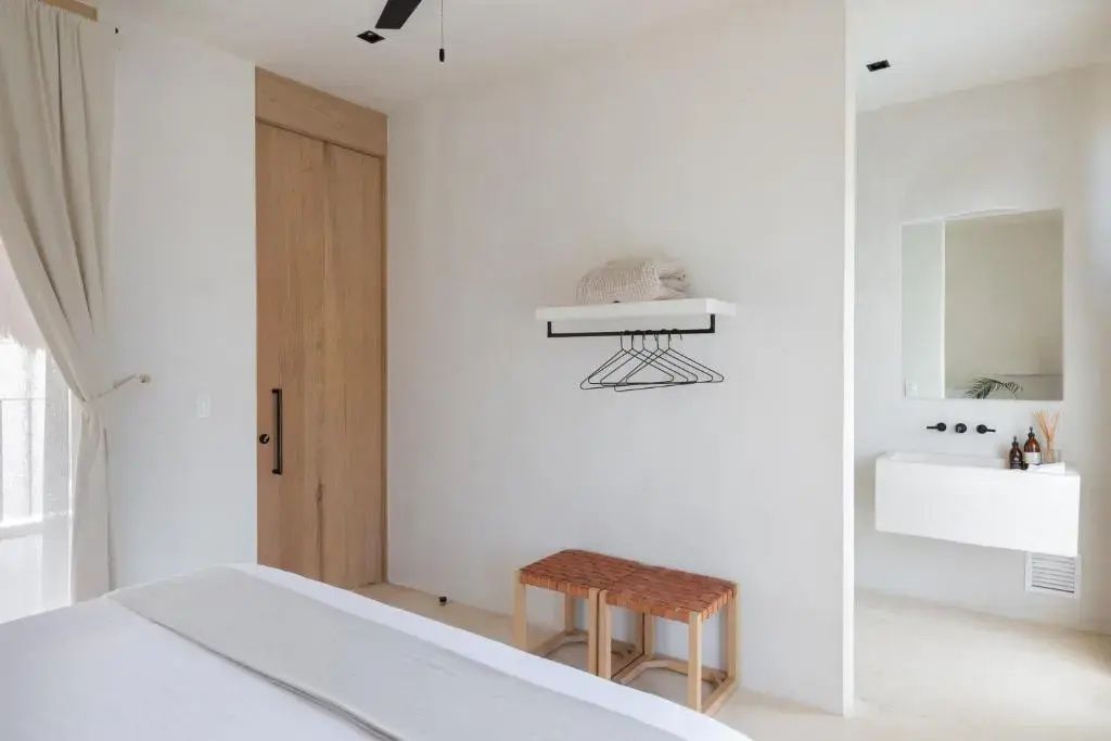 Weißes Hotelzimmer mit hölzerner Schiebetür, Wandregal mit Kleiderbügeln und Hockern.
