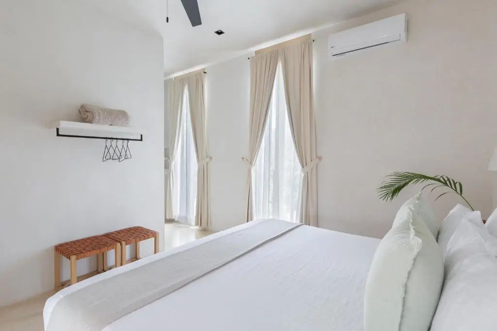 Hell eingerichtetes Schlafzimmer mit großem Bett, bodentiefen Vorhängen und Klimaanlage.