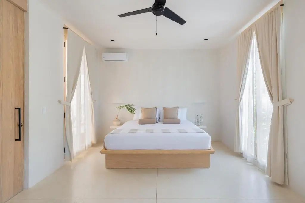 Hell gestaltetes Schlafzimmer mit zentralem Doppelbett und schwarzem Deckenventilator.