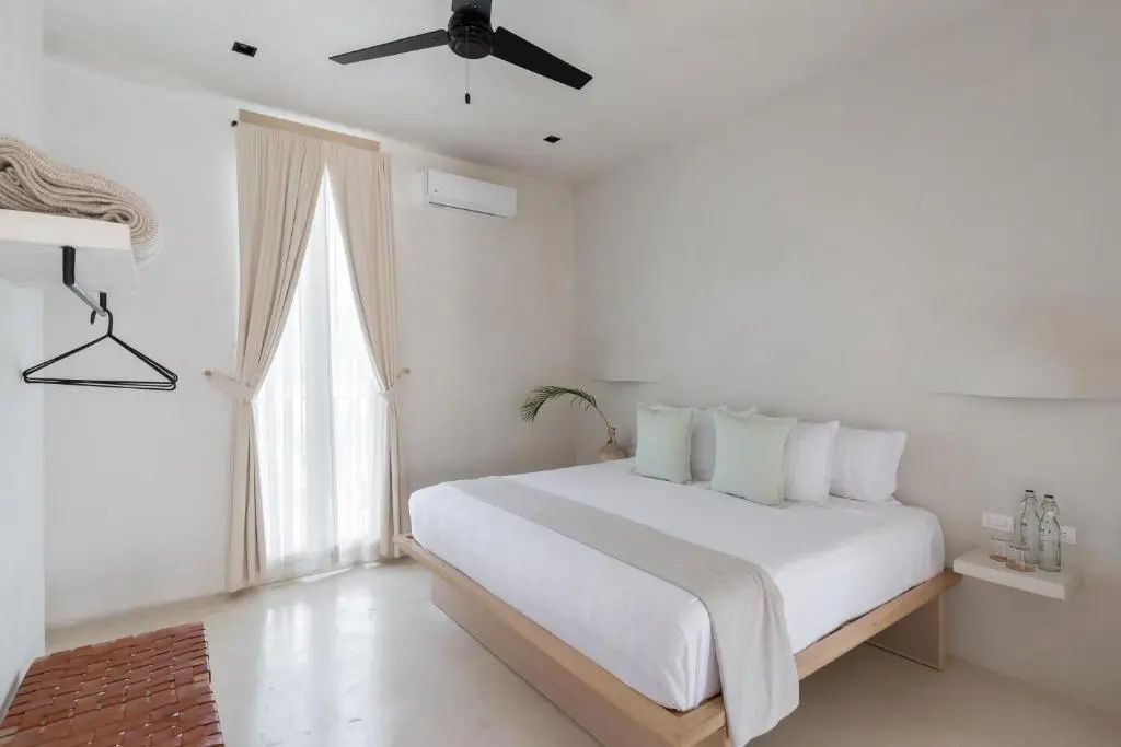 Modernes Hotelzimmer in hellen Tönen mit Doppelbett und schwarzem Ventilator.