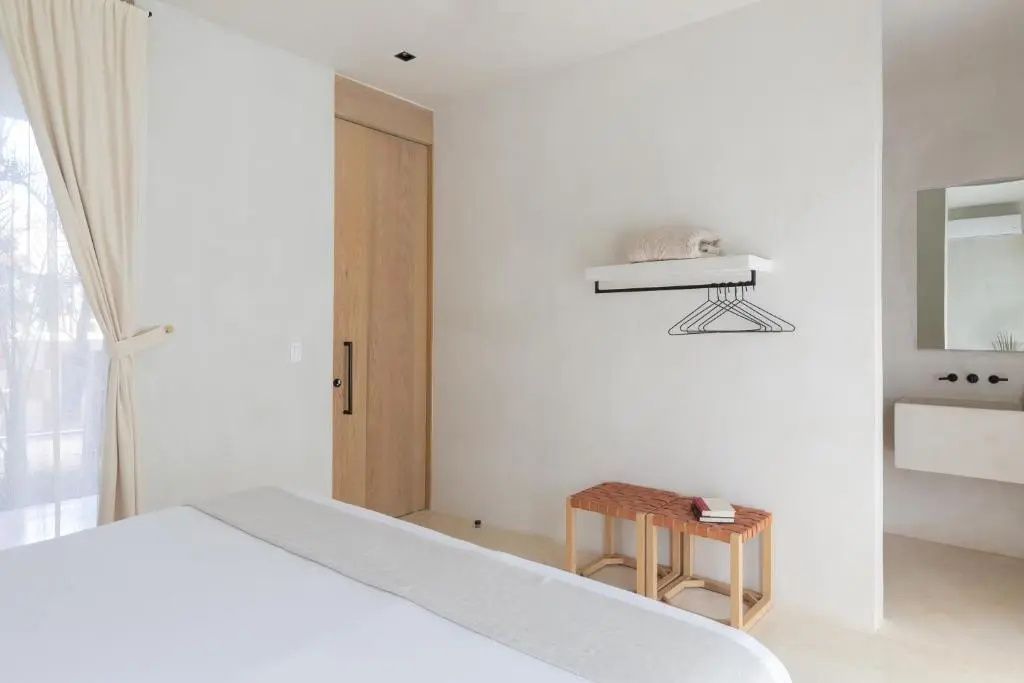 Schlafbereich mit Holztür, Hängegarderobe, Wandregal und zwei geflochtenen Hockerbänken.