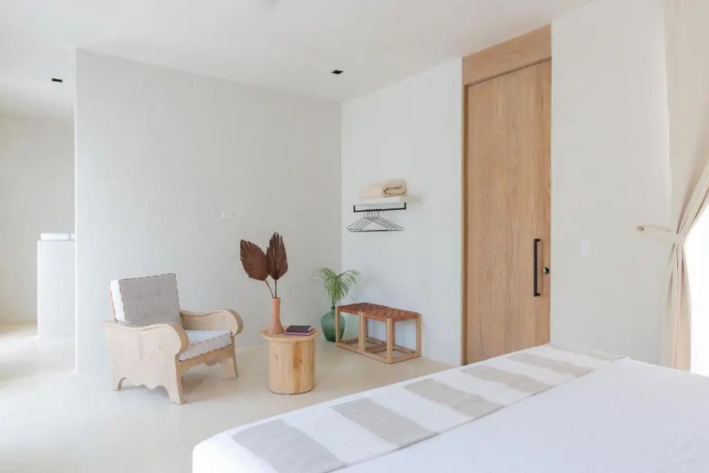 Holzsessel und kleiner Beistelltisch neben einer Sitzbank im schlicht eingerichteten Zimmer.