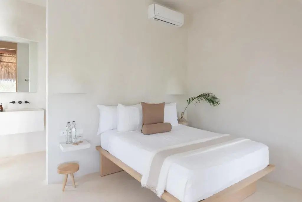 Helles Hotelzimmer mit Doppelbett, weißer Wand, Holzstuhl und Klimaanlage an der Wand.