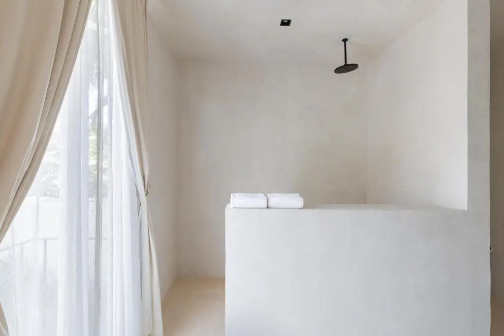 Minimalistisches Badezimmer mit Regendusche, beigefarbenen Wänden und weißen Handtüchern.