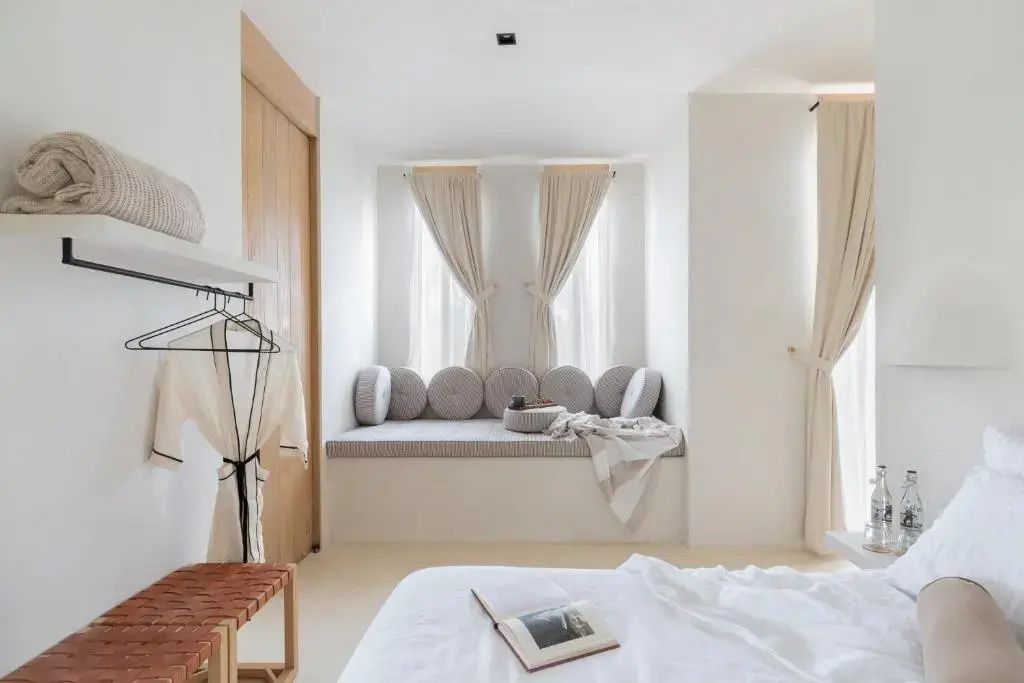 Zimmerbereich mit integrierter Sitzbank am Fenster, Kissen und Bett im Vordergrund.