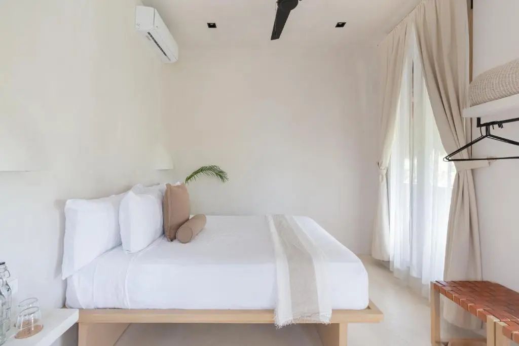 Doppelbett mit weißer Bettwäsche, cremefarbenen Vorhängen und Deckenventilator.
