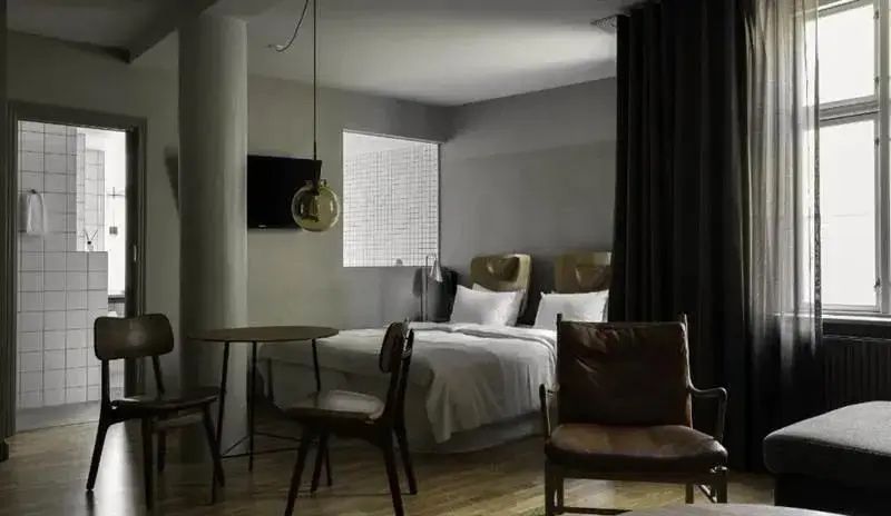 Schlafbereich im Hotelzimmer mit Holzsessel, Tisch und Vorhang.