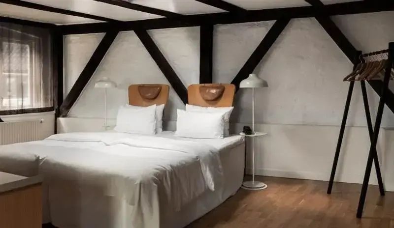 Doppelbett unter einer Dachschräge mit sichtbaren Holzbalken und weißen Stehlampen.