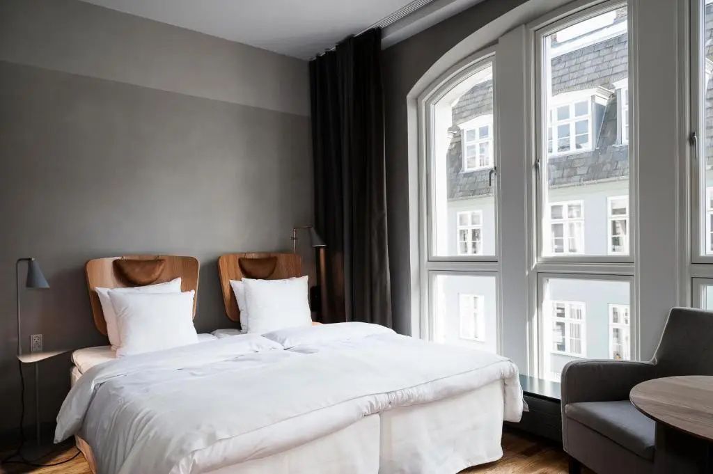 Doppelbett mit weißer Bettwäsche und Holz-Kopfteil neben großen Bogenfenstern