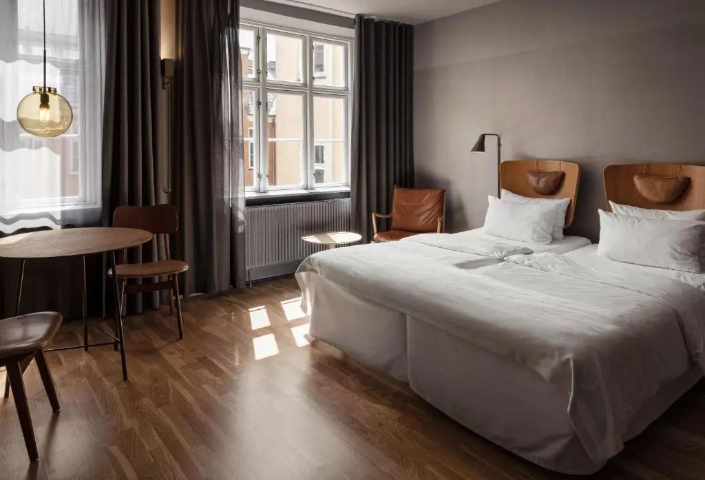 Hotelzimmer mit Parkettboden, großem Doppelbett, braunem Ledersessel und Fenster zur Straße.